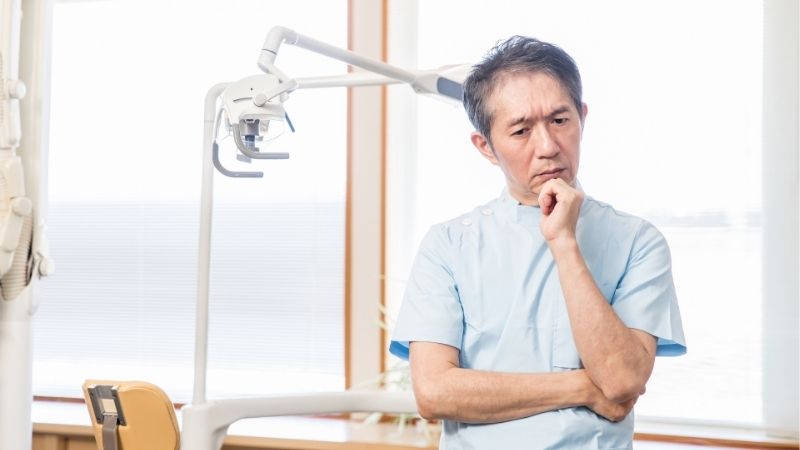 男性歯科医師が顎に手を当てて悩んでいる
